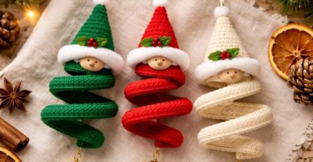 Three crocheted spiraled elf ornaments in green, red, and cream, each with a festive hat, wooden face, and gold bell, displayed on linen with Christmas decor.