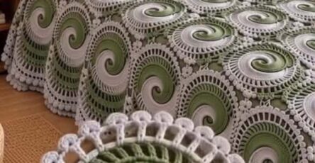 A crocheted bedspread made from joined spiral motifs in sage green and white, shown on a bed with matching pillows.