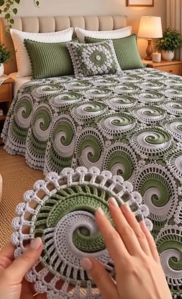 A crocheted bedspread made from joined spiral motifs in sage green and white, shown on a bed with matching pillows.