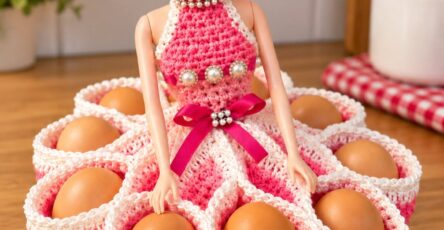 A crocheted egg holder modeled as a doll in a flowing pink and white dress with multiple pockets for eggs.