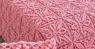 A chunky pink crochet bedspread with star-shaped motifs joined together, draped over a bed with pink and white pillows.