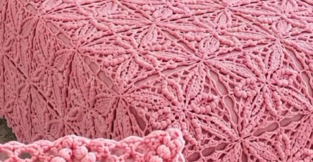 A chunky pink crochet bedspread with star-shaped motifs joined together, draped over a bed with pink and white pillows.