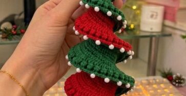 A spiral crochet Christmas tree ornament featuring alternating red and green ruffled layers, white beads, a golden bell, and two yellow stars on top.