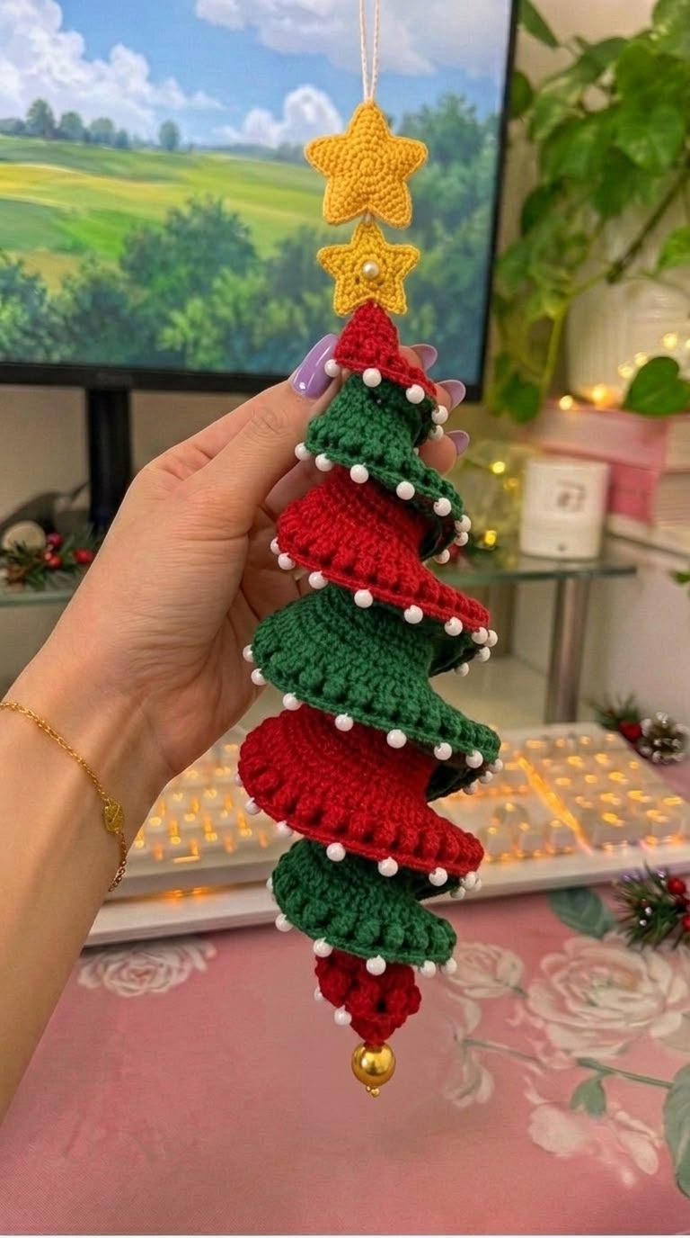 A spiral crochet Christmas tree ornament featuring alternating red and green ruffled layers, white beads, a golden bell, and two yellow stars on top.