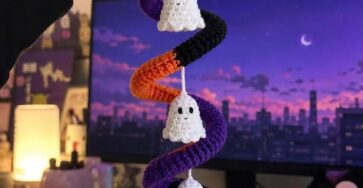 Crocheted spiral garland in purple, orange, and black with four small white ghost ornaments hanging at intervals.