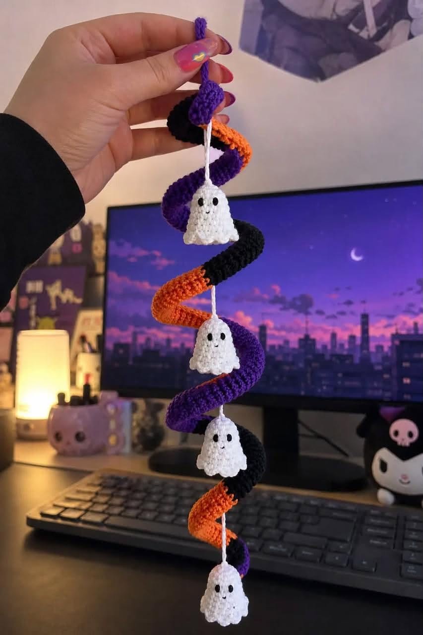 Crocheted spiral garland in purple, orange, and black with four small white ghost ornaments hanging at intervals.