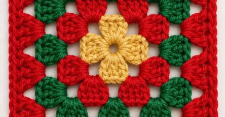 A colorful crochet granny square in yellow, green, and red yarn with a floral center on a white background.