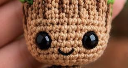 A crocheted amigurumi tree doll keychain with brown body, green leaf accents, and large black safety eyes.