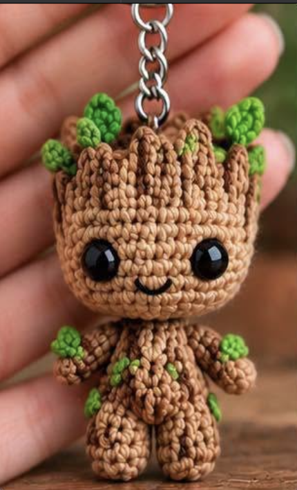 A crocheted amigurumi tree doll keychain with brown body, green leaf accents, and large black safety eyes.