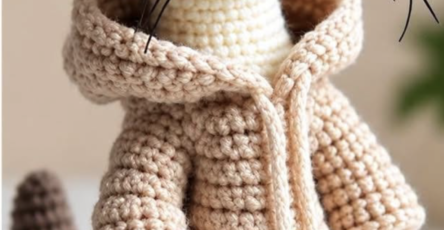 Crocheted ferret amigurumi toy wearing a beige hoodie with realistic whiskers and shaded colorwork.