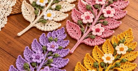 Four crochet fern leaf mats in cream, pink, purple, and yellow, each adorned with green buds and 3D flowers, displayed on a wooden tabletop.