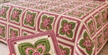 A floral granny square crochet blanket and matching cushion covers with a three-dimensional pink flower and green leaves in each square.