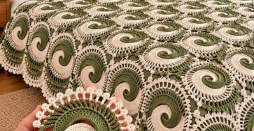 Green and cream swirl motif crochet blanket on a bed, with a hand holding a single motif in the foreground.