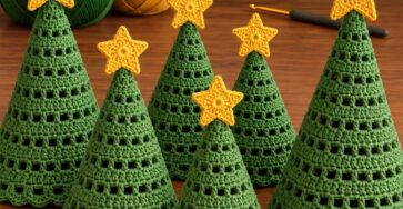 Six crochet Christmas tree cones in green with yellow star toppers, arranged on a wooden surface, with green and yellow yarn and a crochet hook in the background.