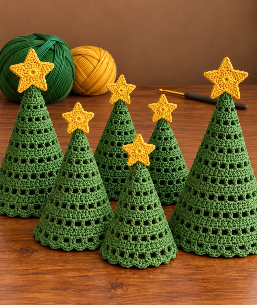 Six crochet Christmas tree cones in green with yellow star toppers, arranged on a wooden surface, with green and yellow yarn and a crochet hook in the background.