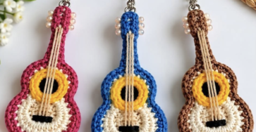 Three crocheted guitar keychains in pink, blue, and brown with realistic details, round bodies, and strung with embroidery thread.