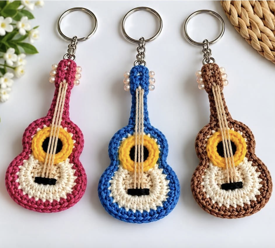 Three crocheted guitar keychains in pink, blue, and brown with realistic details, round bodies, and strung with embroidery thread.