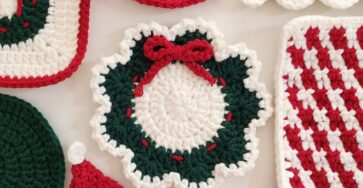 A round crochet holiday wreath appliqué with a scalloped green and white border and a red crocheted bow.