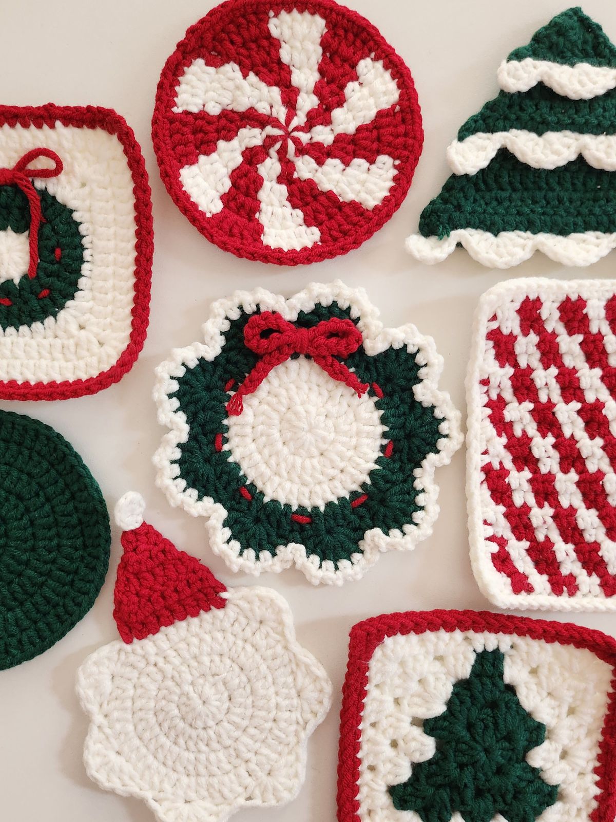 A round crochet holiday wreath appliqué with a scalloped green and white border and a red crocheted bow.